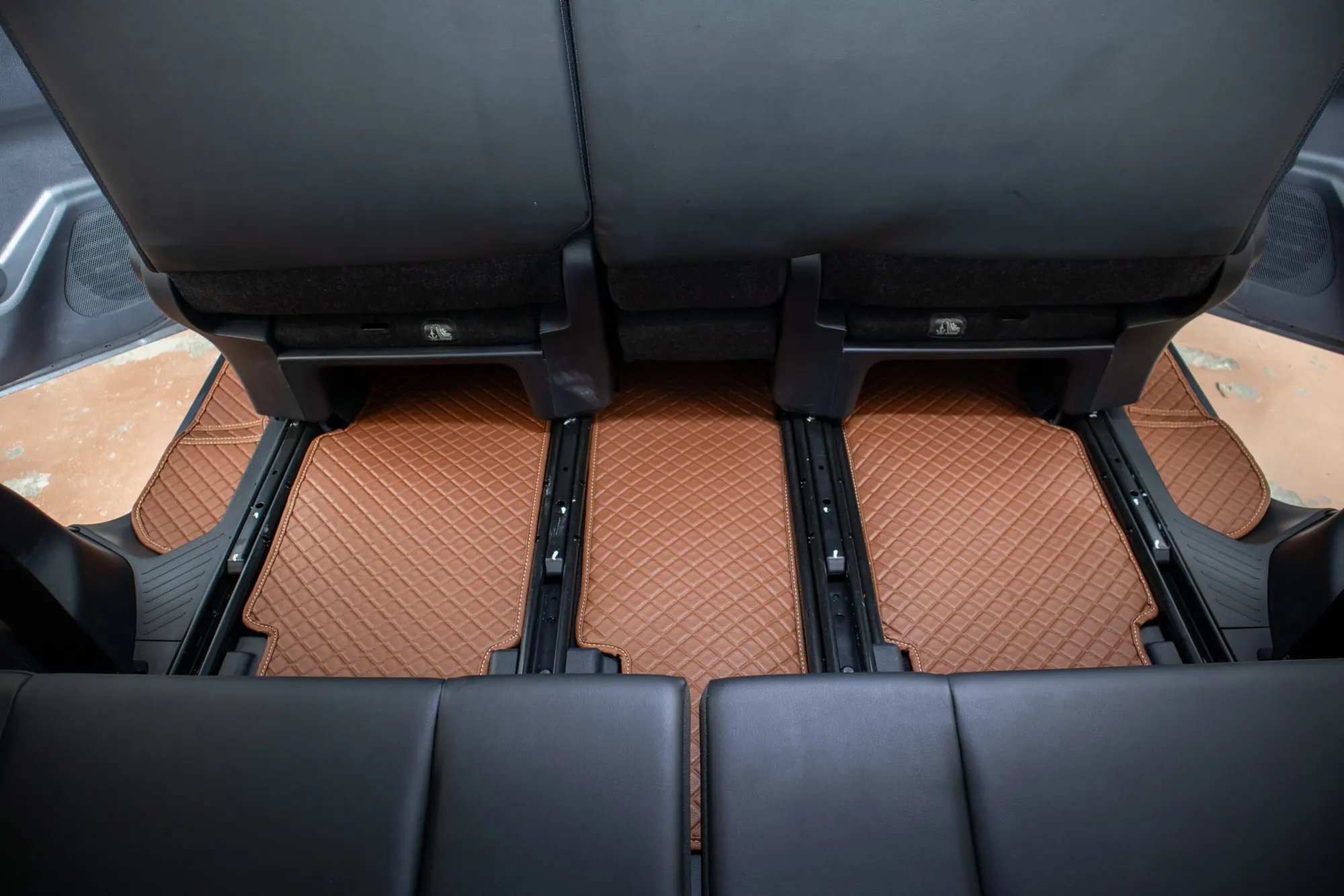 Seat rails of a seven-seater with a tan 3D car mat fitted between them