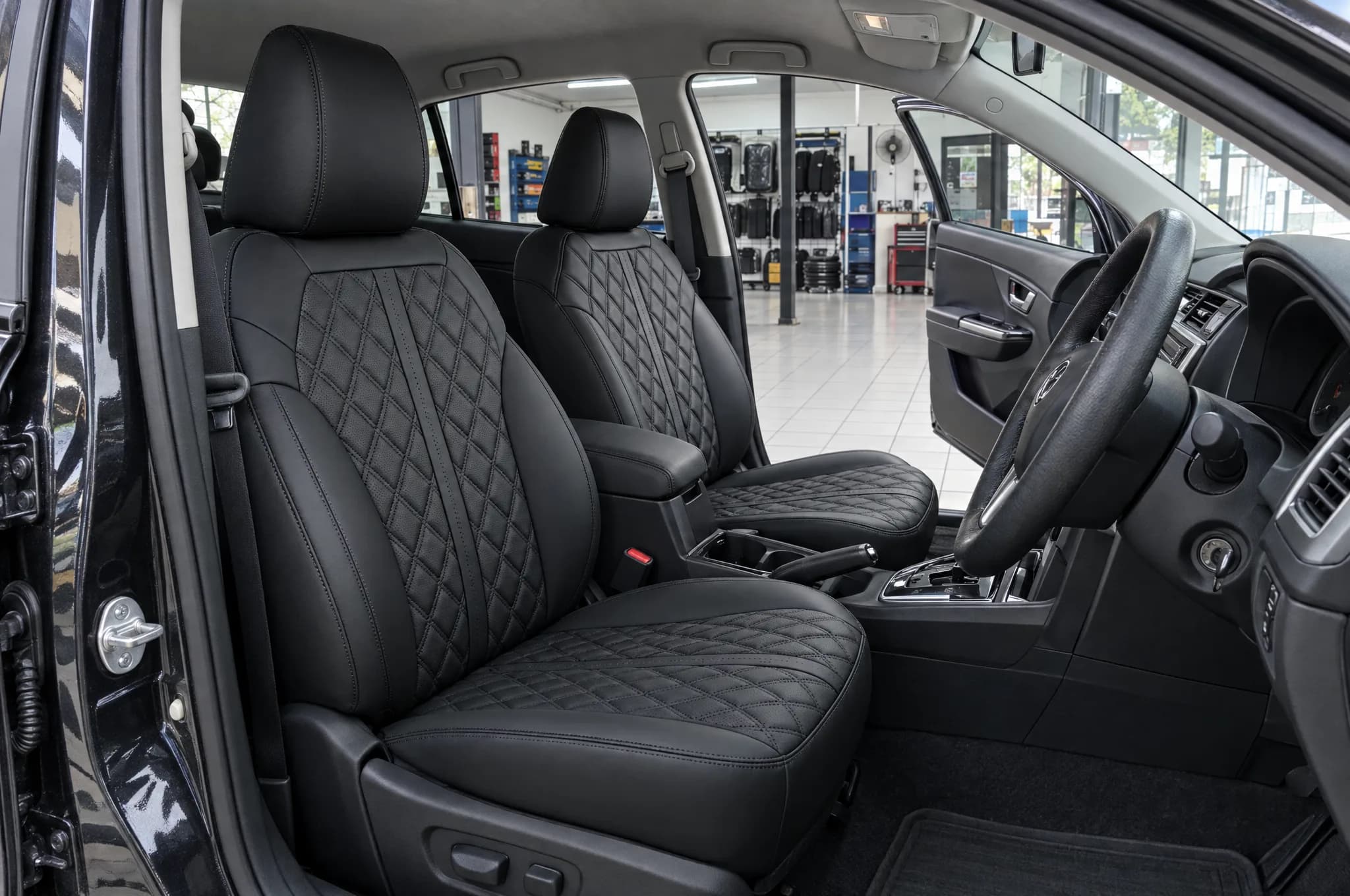 Render: front row of a sedan with black Adamas seat covers, seen through the open door